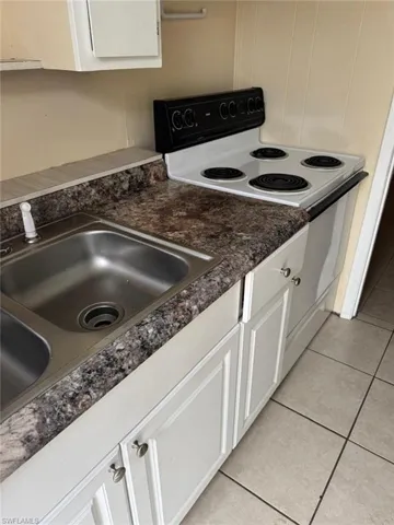 Kitchen with white cabinetry, sink, light tile patterned floors, and white electric range oven