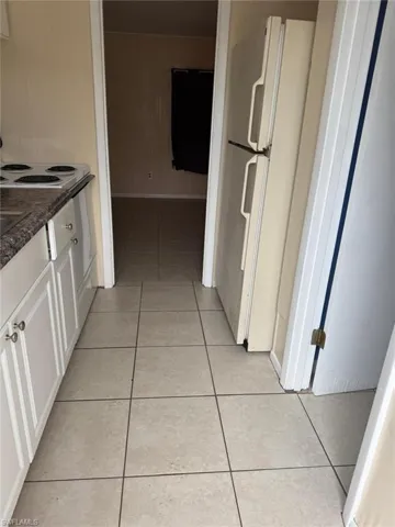Kitchen featuring dark stone counters, white cabinets, light tile patterned floors, and white fridge