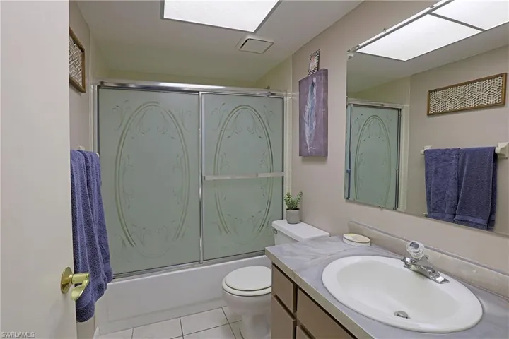 Bathroom featuring a shower-tub combination with sliding frosted glass doors, a vanity with an integrated sink, a large wall-mounted mirror, and tile flooring