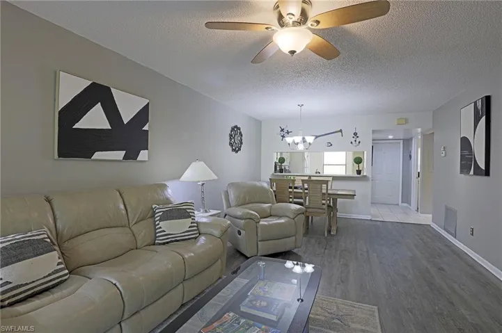 Spacious living area featuring wood-finish flooring, a ceiling fan with integrated lighting, and neutral wall tones
