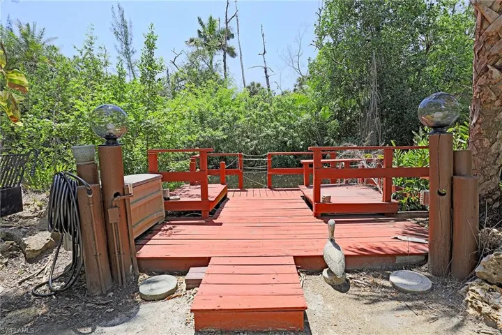 Red-stained wooden dock with railings, featuring two built-in spherical light fixtures and surrounded by lush foliage