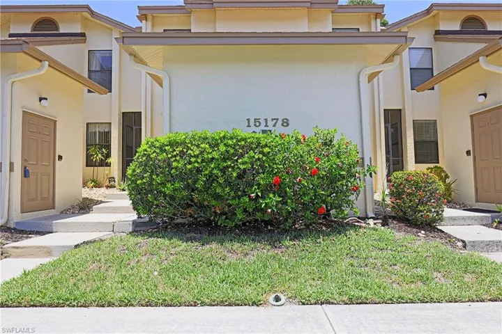 Stucco exterior featuring a prominent central address, covered entryways, symmetrical windows, and manicured shrubbery with red blooms