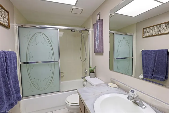 Full bathroom featuring a white bathtub with etched glass sliding doors, a shower head with an attached hose, and white wall tiling