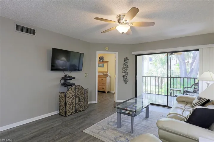 Living area featuring wood-finish flooring, a ceiling fan with integrated lighting, and a glass sliding door providing access to a private balcony
