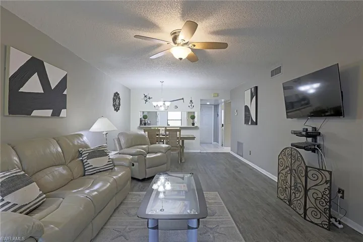 Open-concept living area with wood-finish flooring, neutral wall tones, and a ceiling fan with integrated lighting