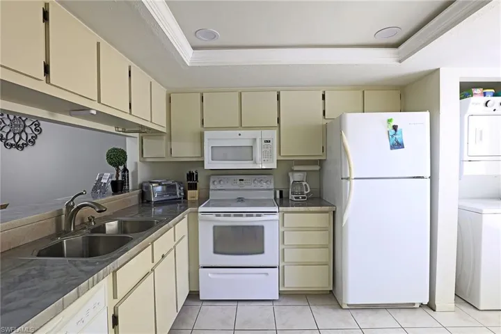Efficient kitchen featuring a double basin stainless steel sink, a white range with an overhead microwave, and a white refrigerator