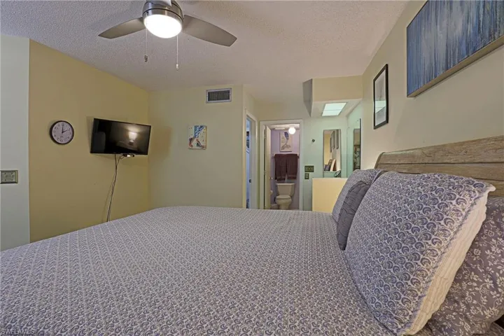 Bedroom featuring a wood-finish headboard, textured ceiling, and a ceiling fan with integrated lighting