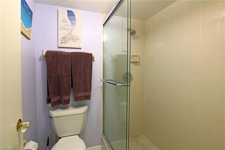 Three-piece bathroom featuring a glass-enclosed shower with tiled walls and a built-in soap dish, a white toilet, and a solid core door with brass hardware