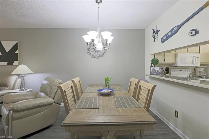 Dining area featuring a contemporary chandelier, wood-finish flooring, and a pass-through window to the kitchen