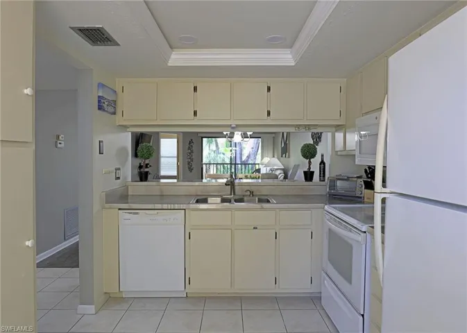 Kitchen featuring white appliances, light-toned cabinetry, and a pass-through window with a mirror backsplash