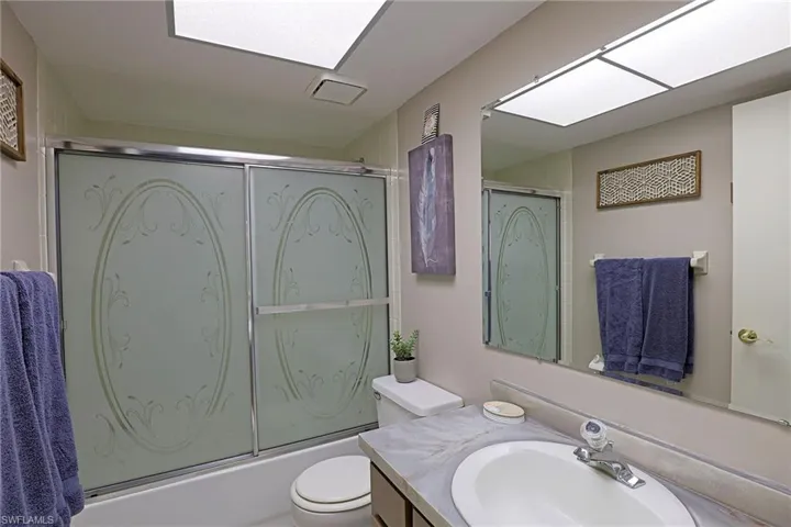 Bathroom featuring a shower-tub combination with patterned frosted glass sliding doors, a vanity with an integrated sink and laminate countertop, and a large wall-mounted mirror