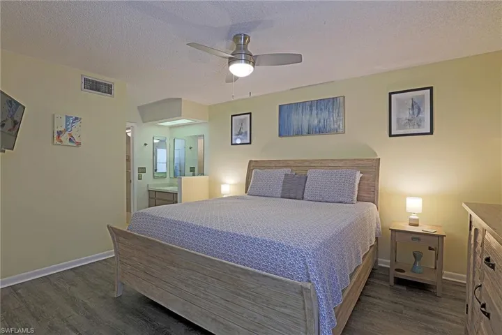 Bedroom featuring wood-finish flooring, a ceiling fan with integrated lighting, and direct access to a bathroom with a dual vanity