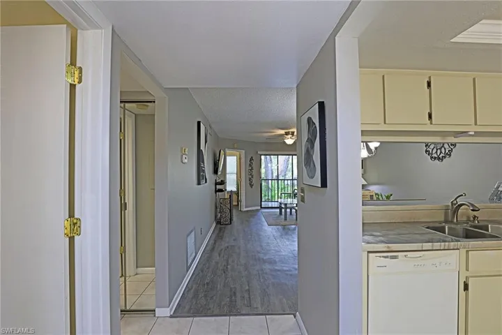 Galley kitchen featuring a dual-basin stainless steel sink, a built-in dishwasher, and light-toned cabinetry, with a pass-through opening to the living area