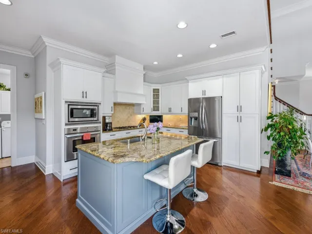 Kitchen featuring light stone counters, stainless steel appliances, an island with sink, crown molding, and glass insert cabinets