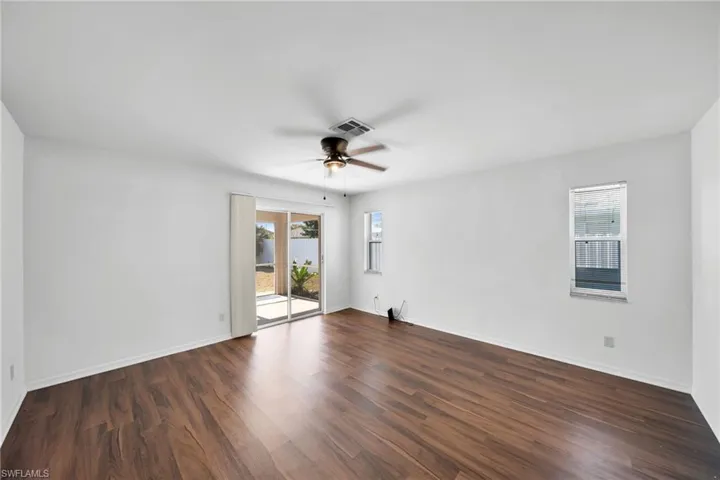 Empty room featuring dark wood-style floors, plenty of natural light, and a ceiling fan