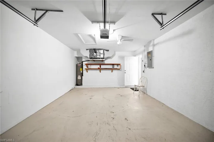 Garage with electric panel, water heater, a textured wall, and a garage door opener