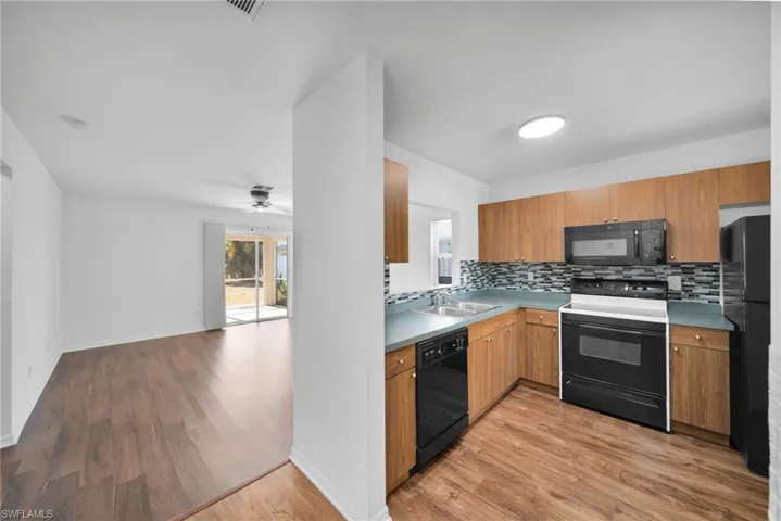 Kitchen featuring black appliances, wood finish cabinetry, light wood-style flooring, and tasteful backsplash