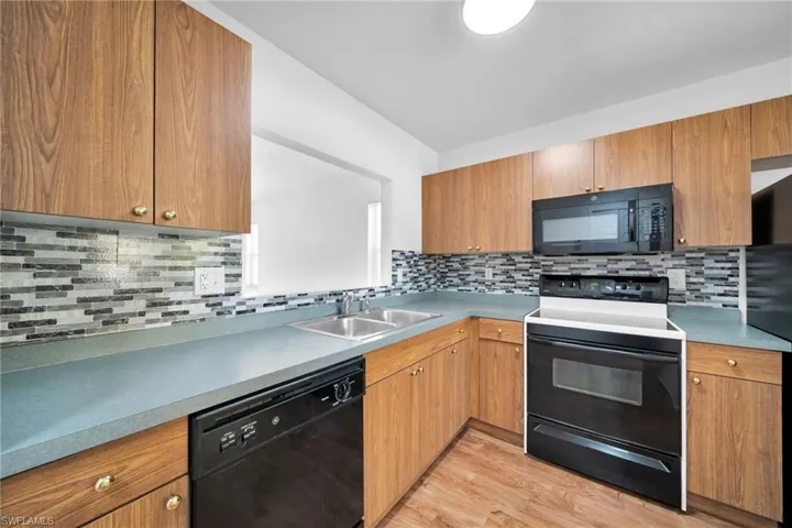 Kitchen featuring black appliances, wood finish cabinetry, backsplash, light wood-style flooring, and light countertops