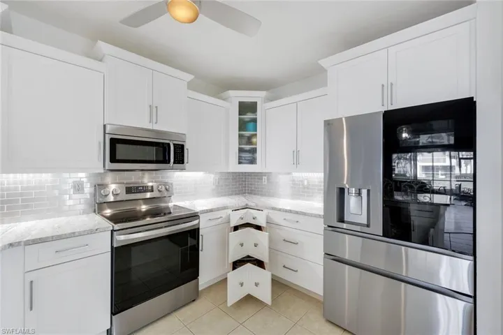 Kitchen with appliances with stainless steel finishes, white cabinets, glass insert cabinets, and light stone countertops