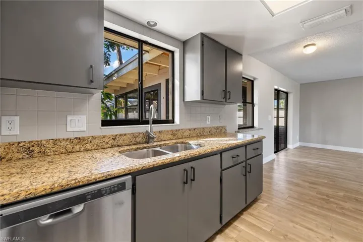 Kitchen with light hardwood / wood-style floors, plenty of natural light, stainless steel dishwasher, and sink