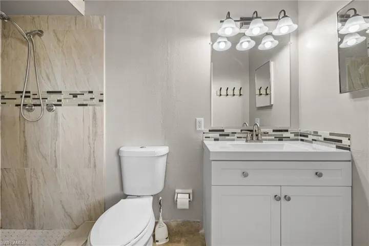 Bathroom with vanity, toilet, tiled shower, and tasteful backsplash