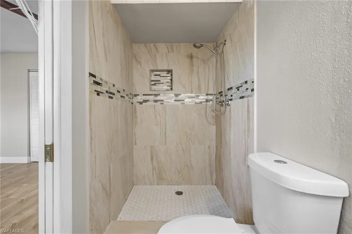 Bathroom featuring hardwood / wood-style flooring, toilet, and a tile shower