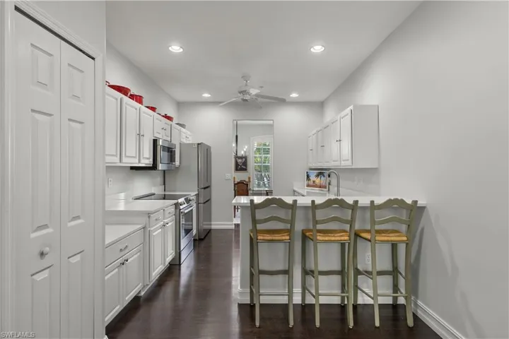 Kitchen featuring dark wood-type flooring, kitchen peninsula, white cabinets, a kitchen bar, and appliances with stainless steel finishes