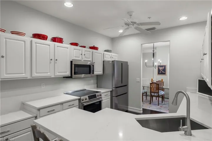 Kitchen featuring sink, white cabinets, stainless steel appliances, and ceiling fan with notable chandelier