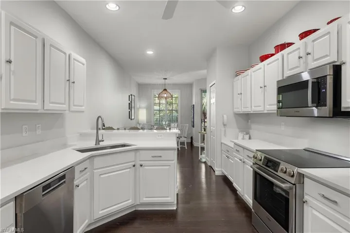 Kitchen with dark wood-type flooring, sink, white cabinets, decorative light fixtures, and appliances with stainless steel finishes