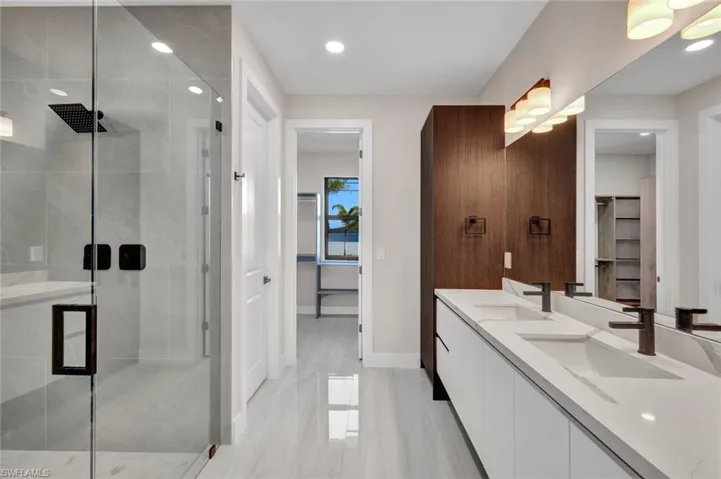 Full bath with a walk in closet, a stall shower, double vanity, and recessed lighting