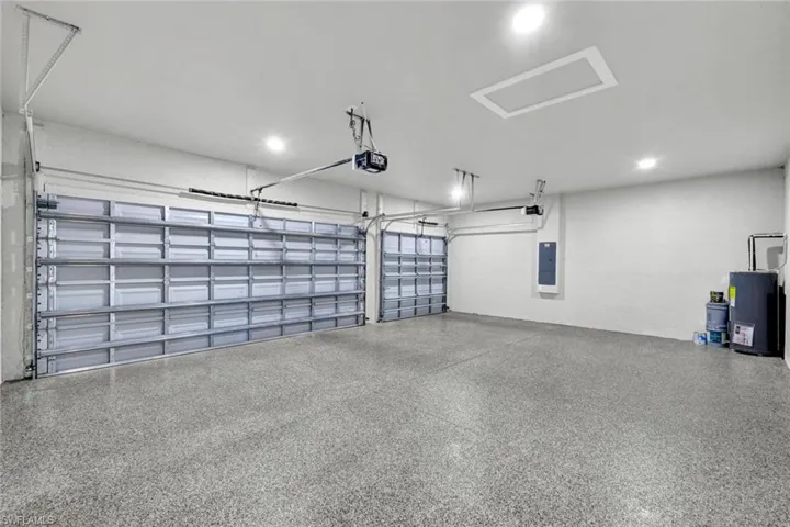 Garage featuring water heater, electric panel, recessed lighting, and a garage door opener