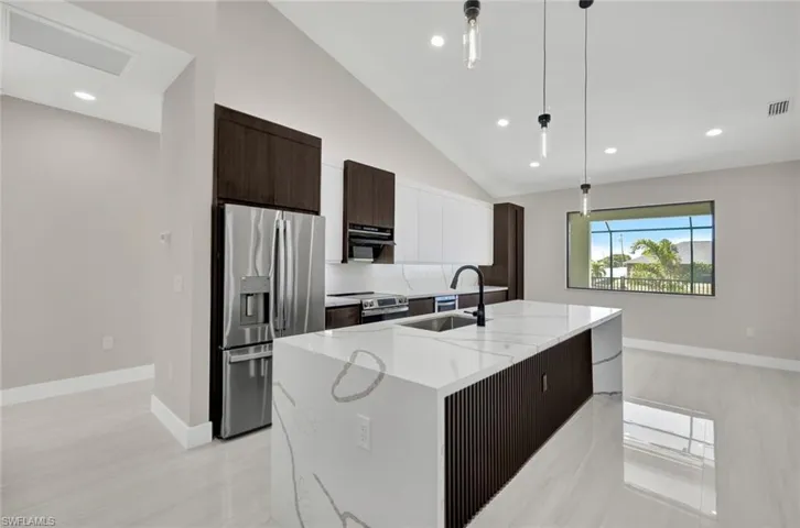 Kitchen featuring modern cabinets, dark brown cabinetry, appliances with stainless steel finishes, pendant lighting, and a kitchen island with sink