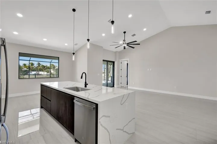 Kitchen featuring dark brown cabinets, modern cabinets, appliances with stainless steel finishes, light stone countertops, and an island with sink