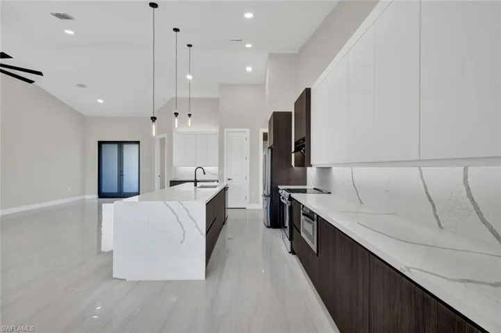 Kitchen with modern cabinets, dark brown cabinetry, light stone countertops, hanging light fixtures, and white cabinets
