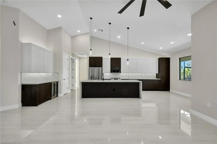 Kitchen with modern cabinets, dark brown cabinetry, a spacious island, high vaulted ceiling, and stainless steel refrigerator with ice dispenser
