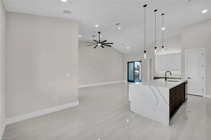 Kitchen featuring hanging light fixtures, high vaulted ceiling, light stone countertops, a center island with sink, and open floor plan