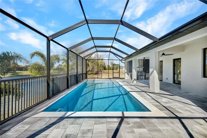 View of swimming pool featuring glass enclosure, a sunroom, an outdoor kitchen, and a patio area