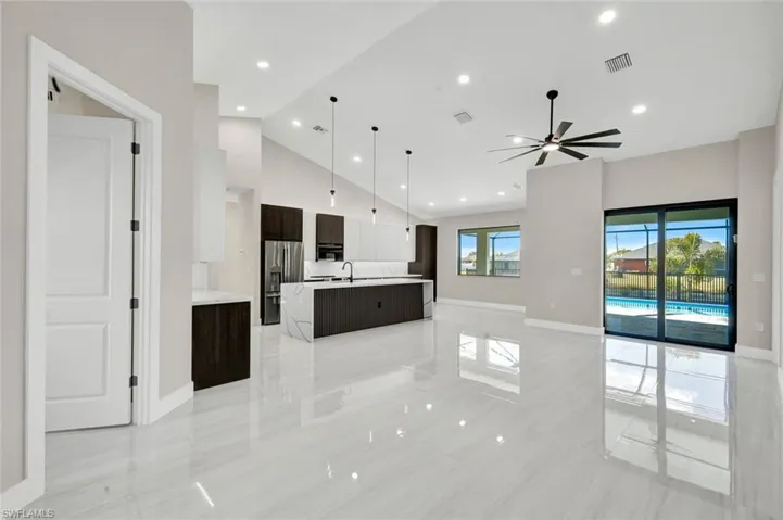 Kitchen with open floor plan, a large island with sink, high vaulted ceiling, dark brown cabinetry, and decorative light fixtures