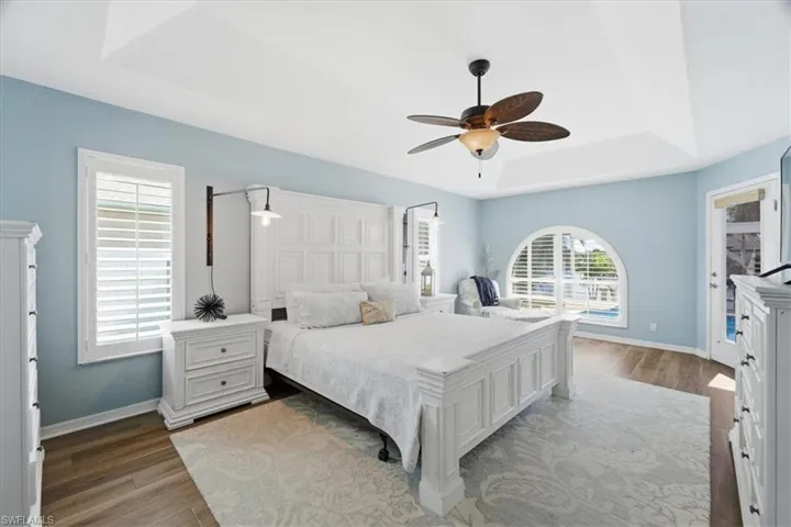 Bedroom with a tray ceiling, wood finished floors, and multiple windows