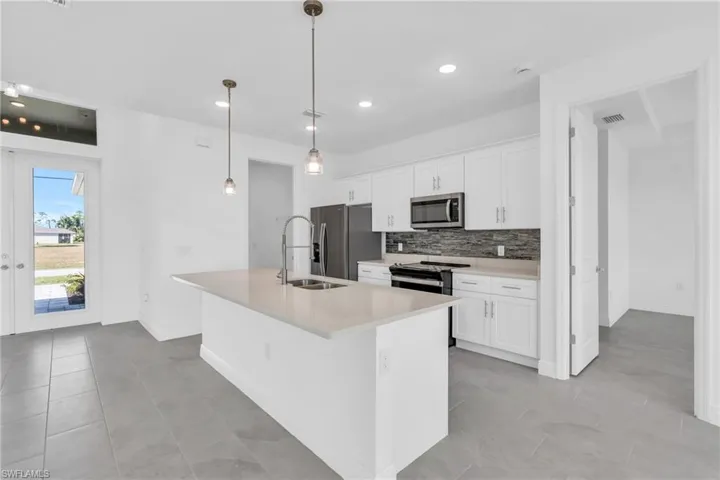 Kitchen featuring white cabinets, sink, hanging light fixtures, an island with sink, and stainless steel appliances