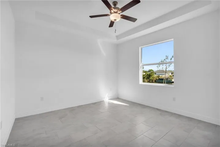 Empty room featuring light tile patterned floors, a raised ceiling, and ceiling fan