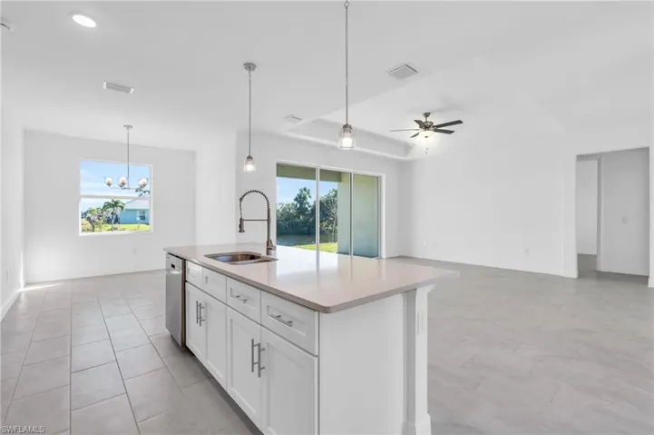 Kitchen featuring white cabinetry, sink, stainless steel dishwasher, a center island with sink, and ceiling fan with notable chandelier