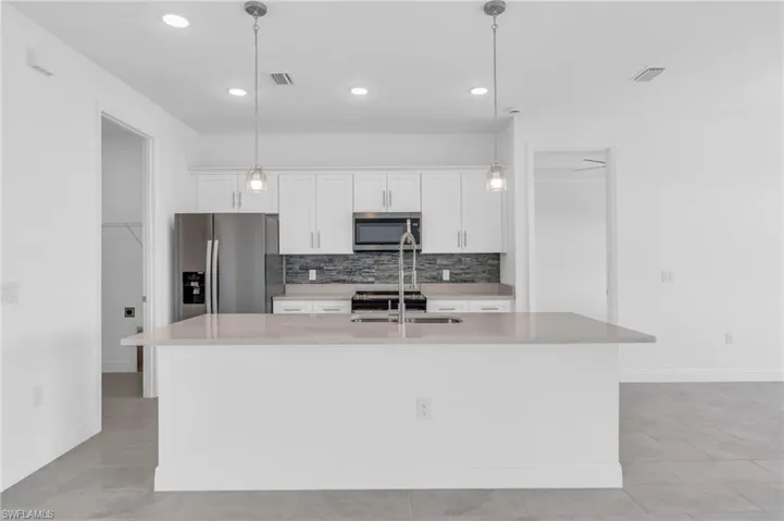 Kitchen with white cabinetry, a kitchen island with sink, pendant lighting, and stainless steel appliances