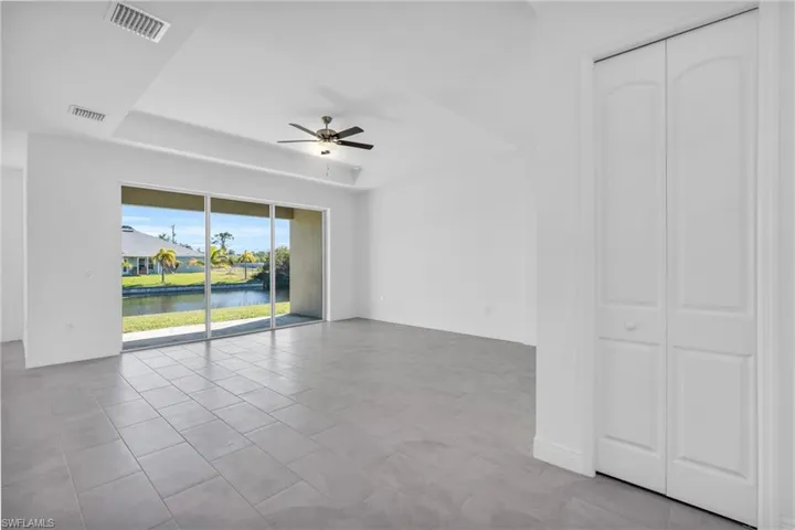 Tiled empty room with a water view, ceiling fan, and a tray ceiling