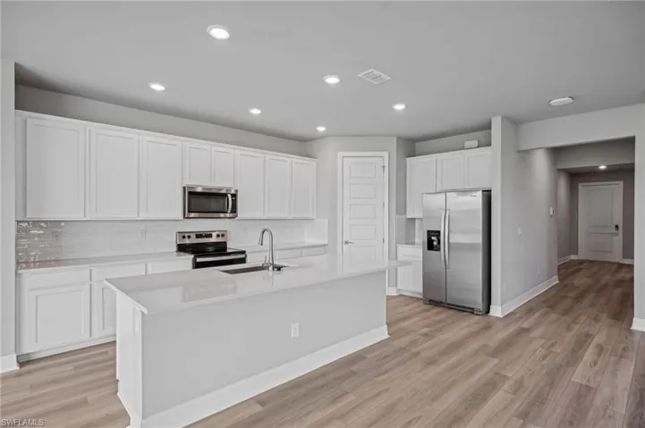 Kitchen with light hardwood / wood-style floors, sink, white cabinetry, a center island with sink, and appliances with stainless steel finishes