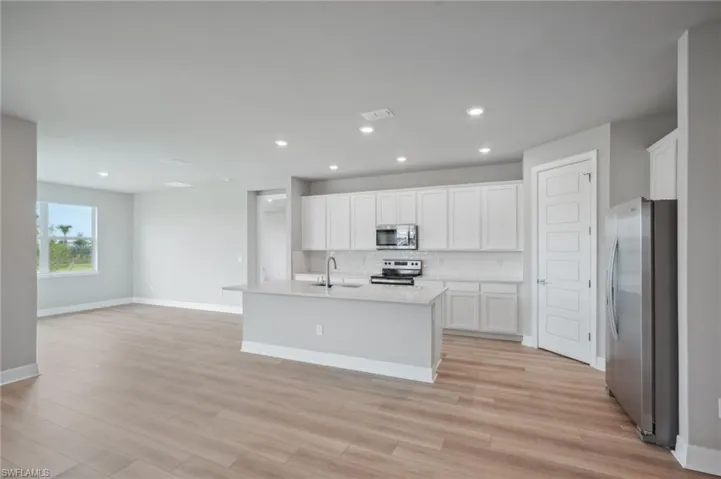 Kitchen with a kitchen island with sink, sink, white cabinetry, light hardwood / wood-style flooring, and appliances with stainless steel finishes