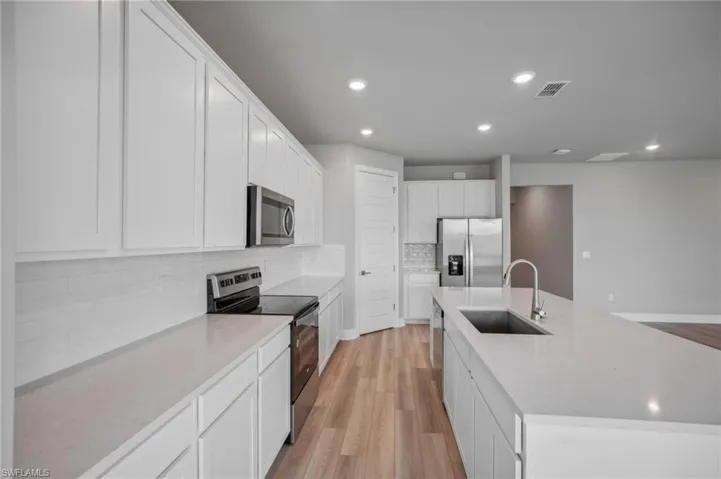 Kitchen featuring a large island with sink, white cabinetry, stainless steel appliances, light hardwood / wood-style flooring, and sink