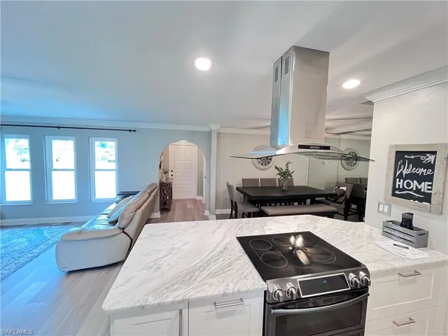 Kitchen with stainless steel range with electric stovetop, arched walkways, island range hood, ornamental molding, and wood finished floors
