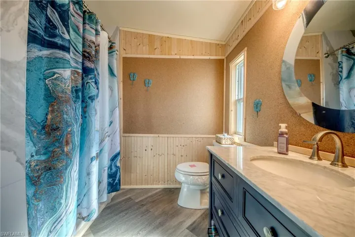 Full bath with wood walls, a shower with shower curtain, vanity, light wood-style floors, and a wainscoted wall