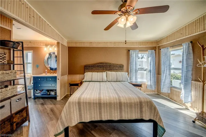 Bedroom with wooden walls, a wainscoted wall, hardwood / wood-style floors, a ceiling fan, and wallpapered walls